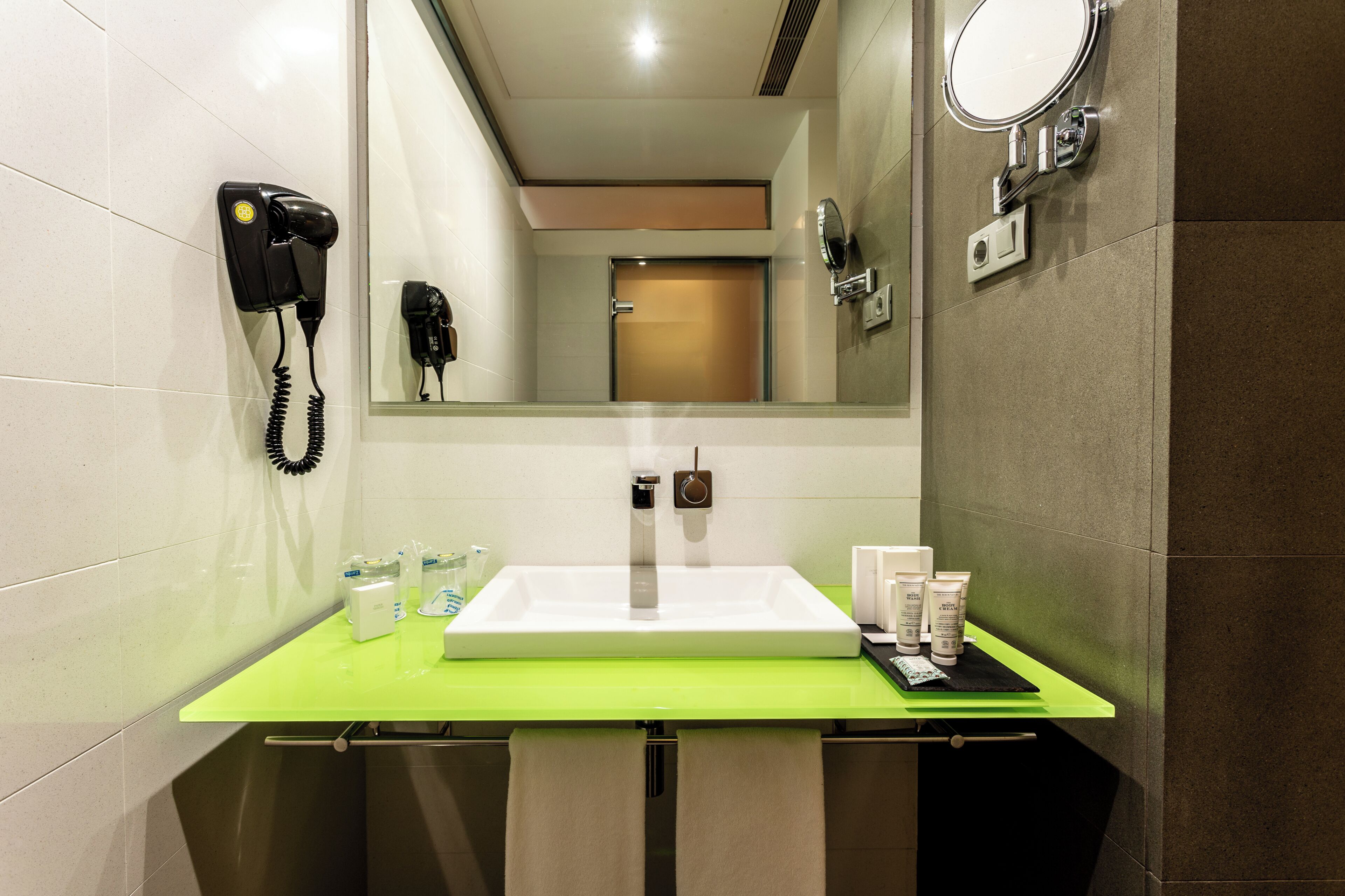 A bathroom with a sink, mirror, hairdryer, and toiletries.