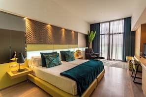 A modern hotel room with a bed, bedside table, lamp, chair, desk, and large window. - La Finca Resort (Algorfa)