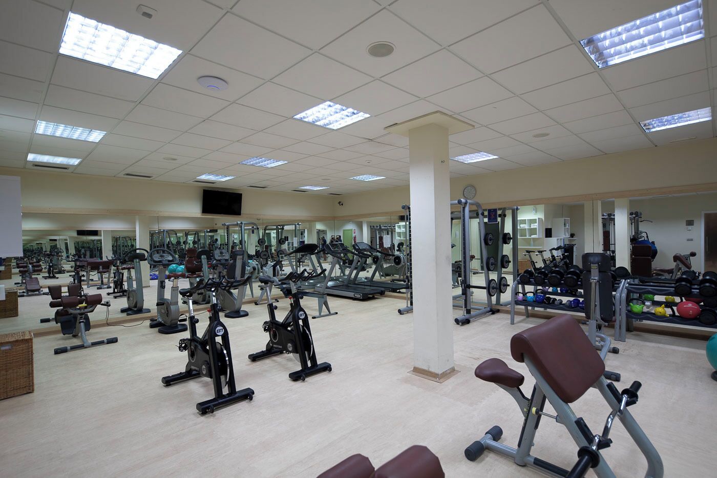 A gym with various exercise equipment, mirrors, and a light-colored floor.