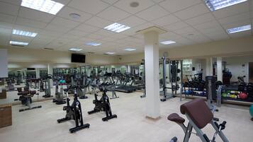 A gym with various exercise equipment, mirrors, and a light-colored floor.
