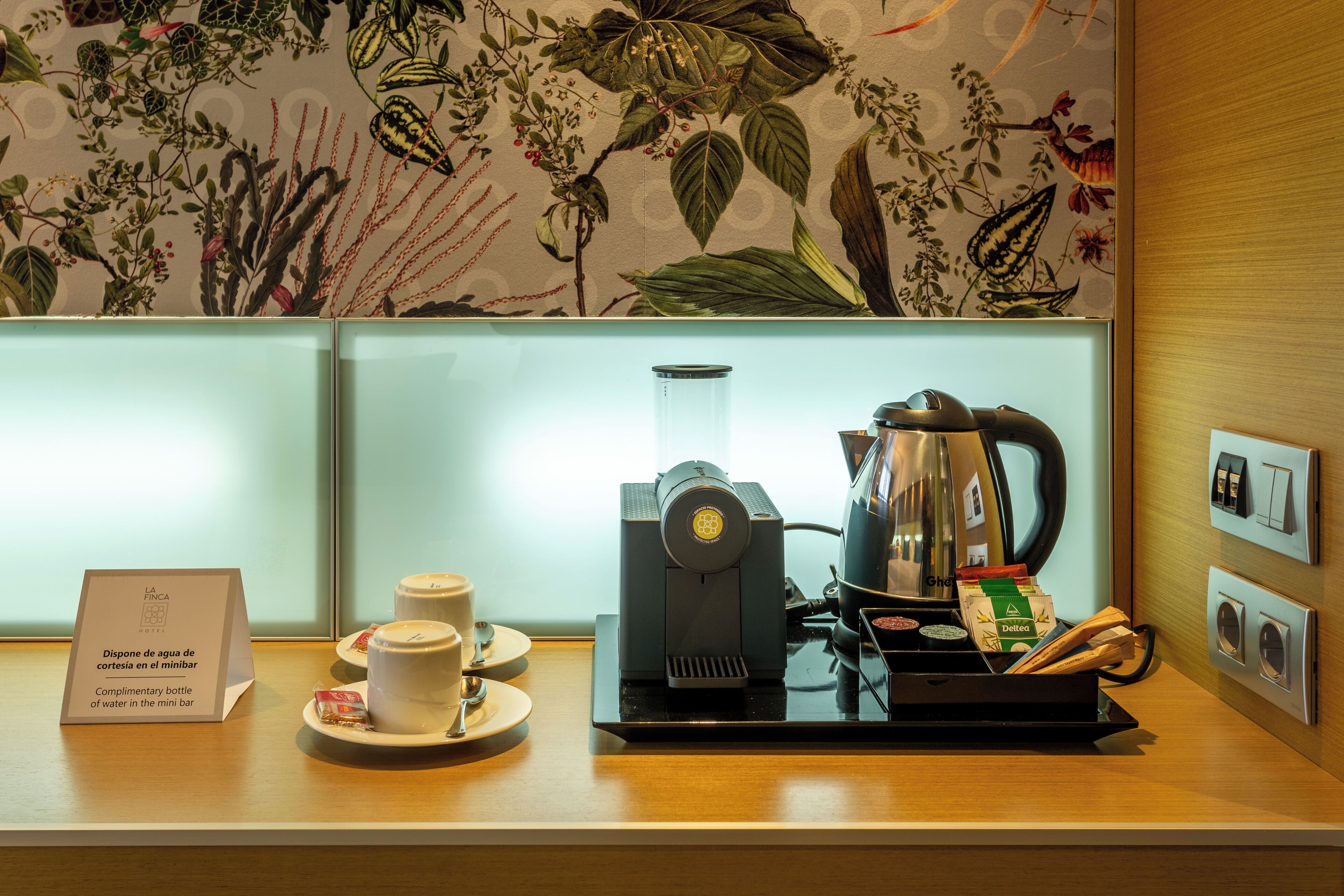 Una macchina da caffè, una tazza, un vassoio e un cartello su un bancone con carta da parati a motivi floreali.