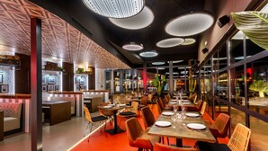 Un restaurante moderno con mesas compartidas largas, sillas acolchadas e iluminación colgante.