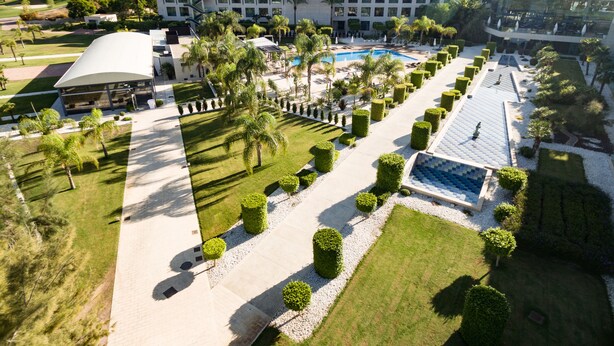 Vista aérea de un hotel con piscina, césped impecable y un edificio grande con múltiples ventanas.