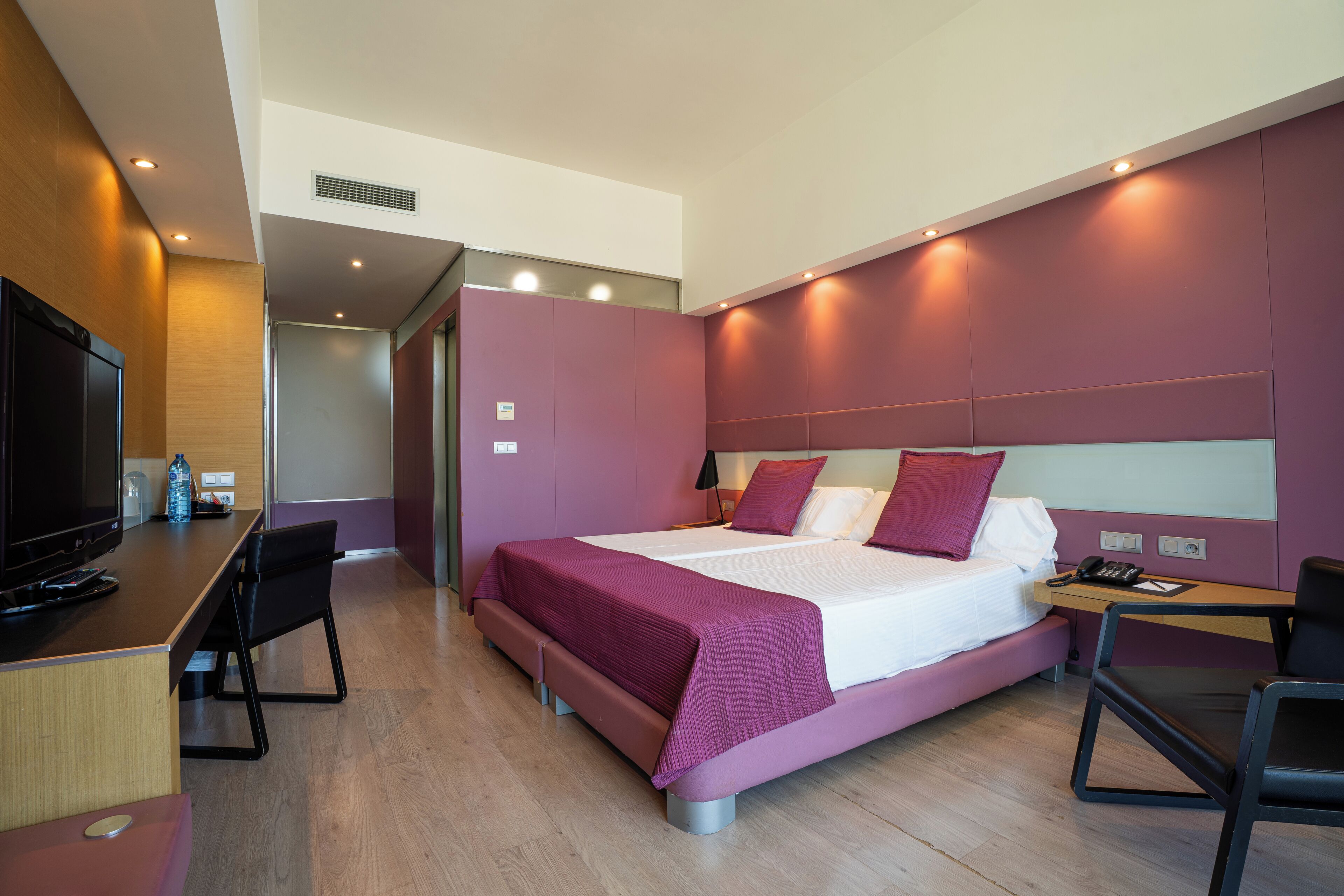 Una habitación de hotel moderna con cama, escritorio, sillas y televisión.