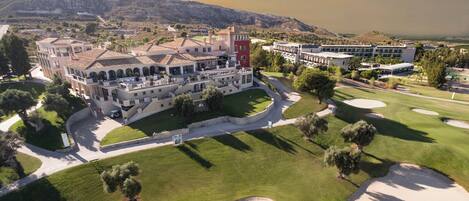 Um hotel grande com vários edifícios, campo de golfe e montanhas ao fundo.