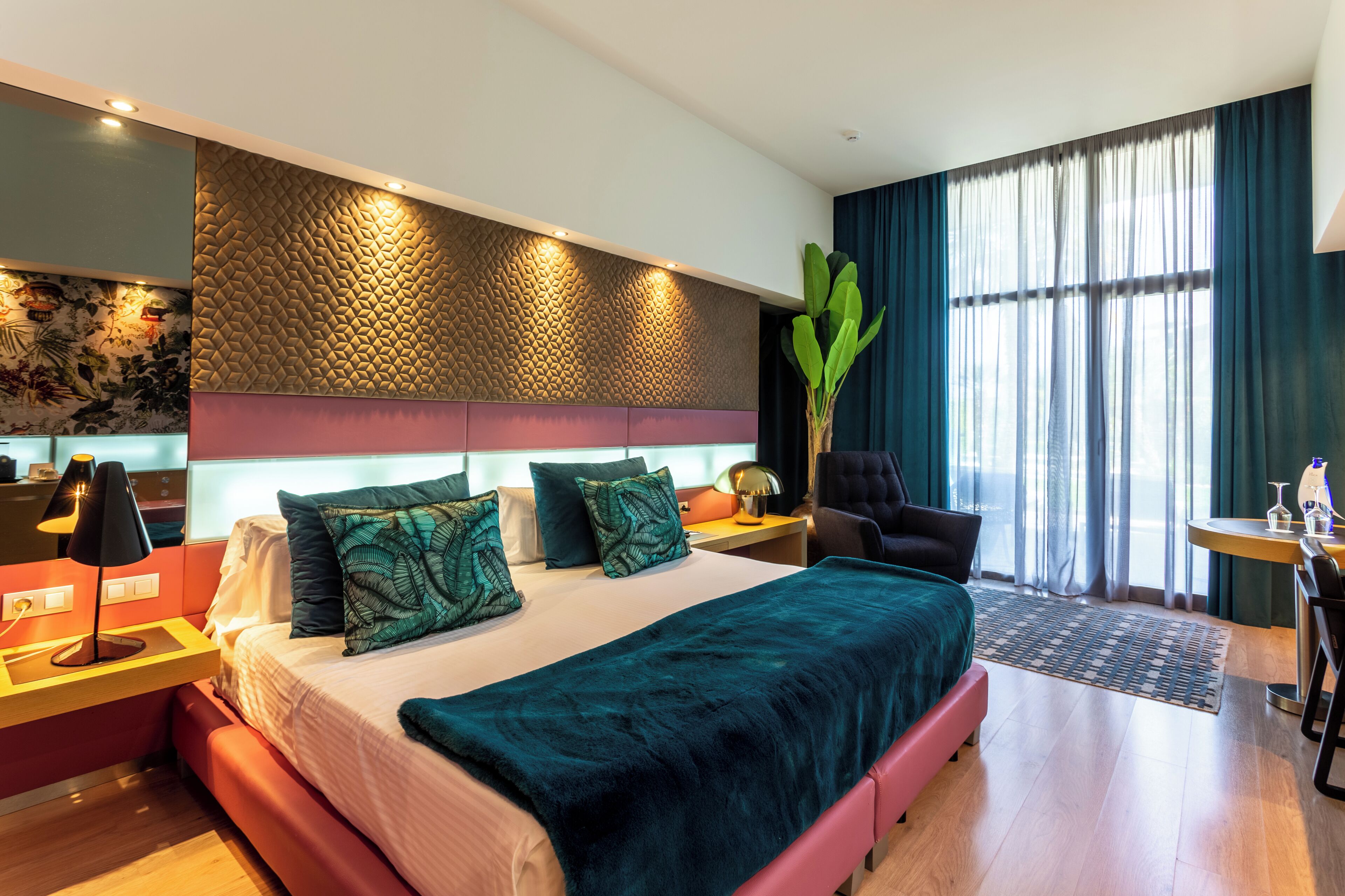 Een moderne hotelkamer met een groot bed, een bureau, een stoel en een groot raam met gordijnen.