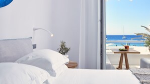 Un dormitorio moderno con una cama grande, una mesita de noche con una planta y vistas al mar desde un balcón.