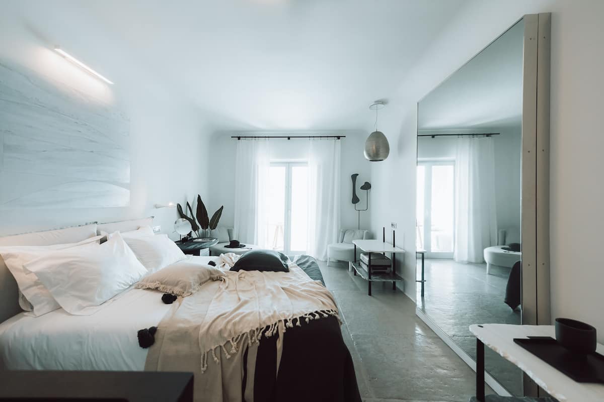 A modern bedroom with a large bed, bedside tables, a desk, and a mirror.