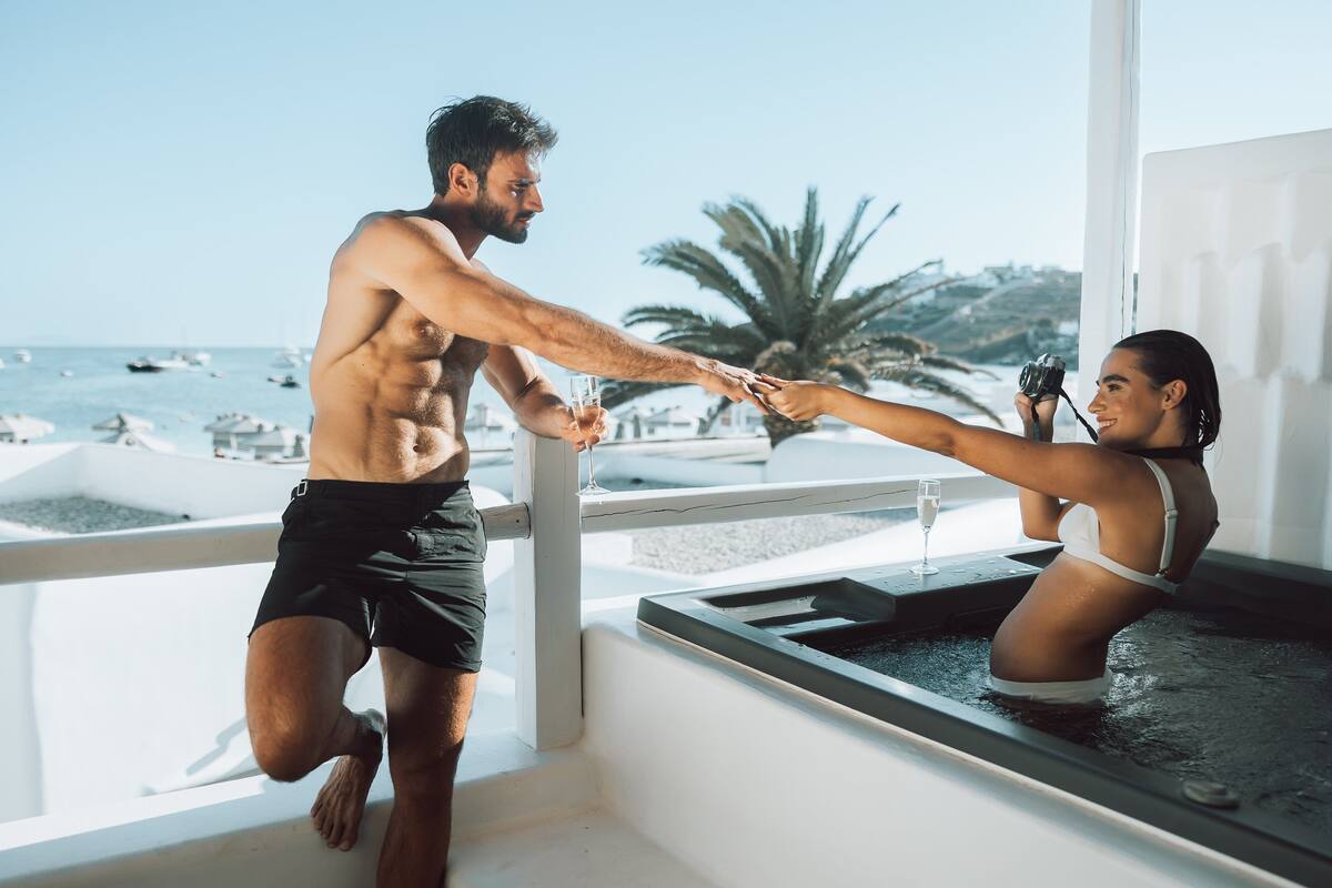 A man and a woman in a hot tub with a view of the sea and palm trees.