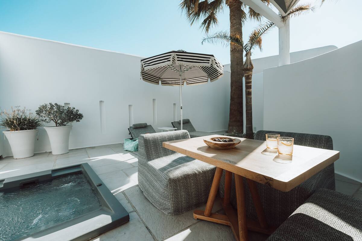 A modern outdoor seating area with a wooden table, striped umbrella, and potted plants.