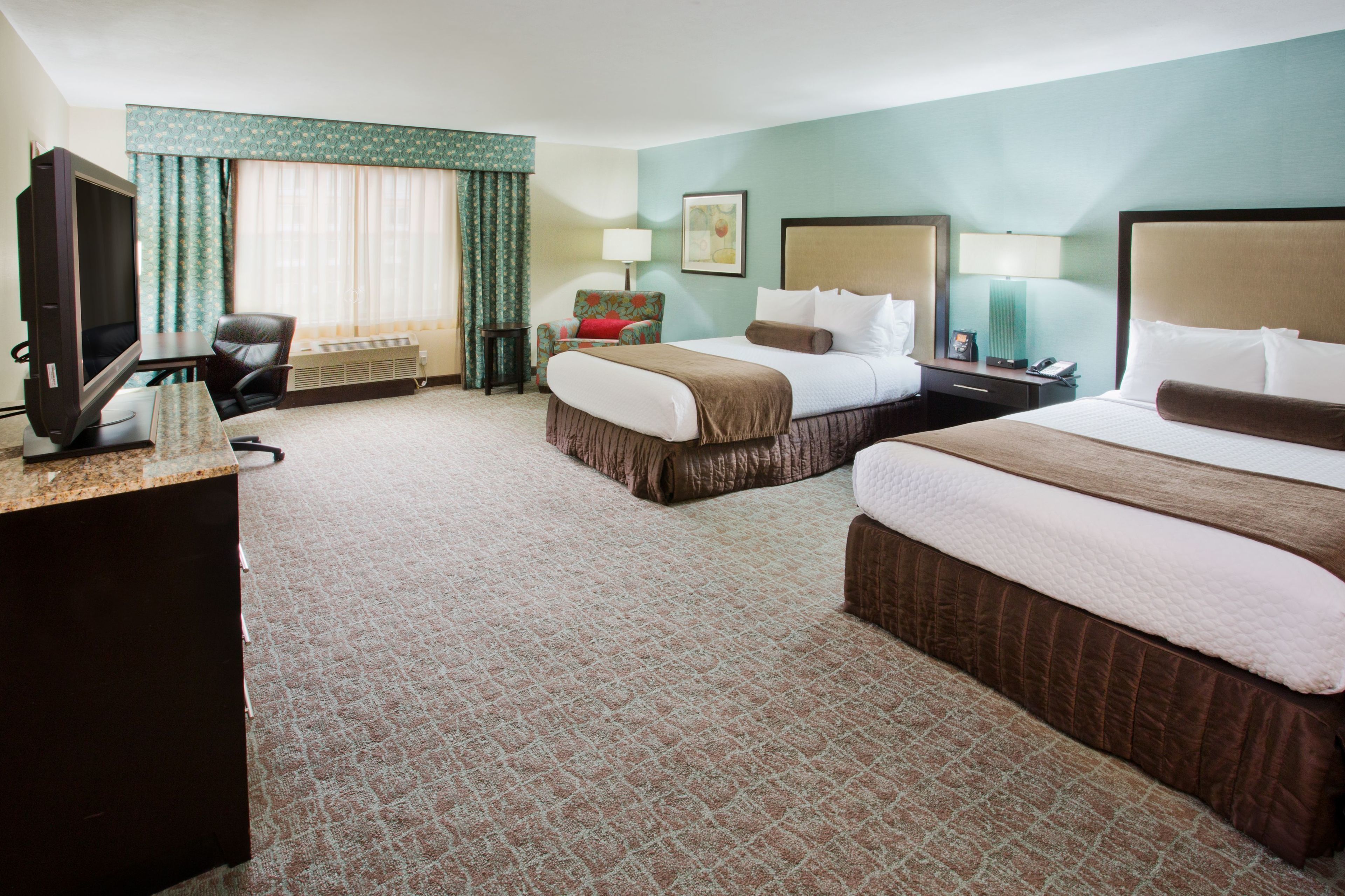 A hotel room with two beds, a desk with a television, a chair, and a window with curtains.