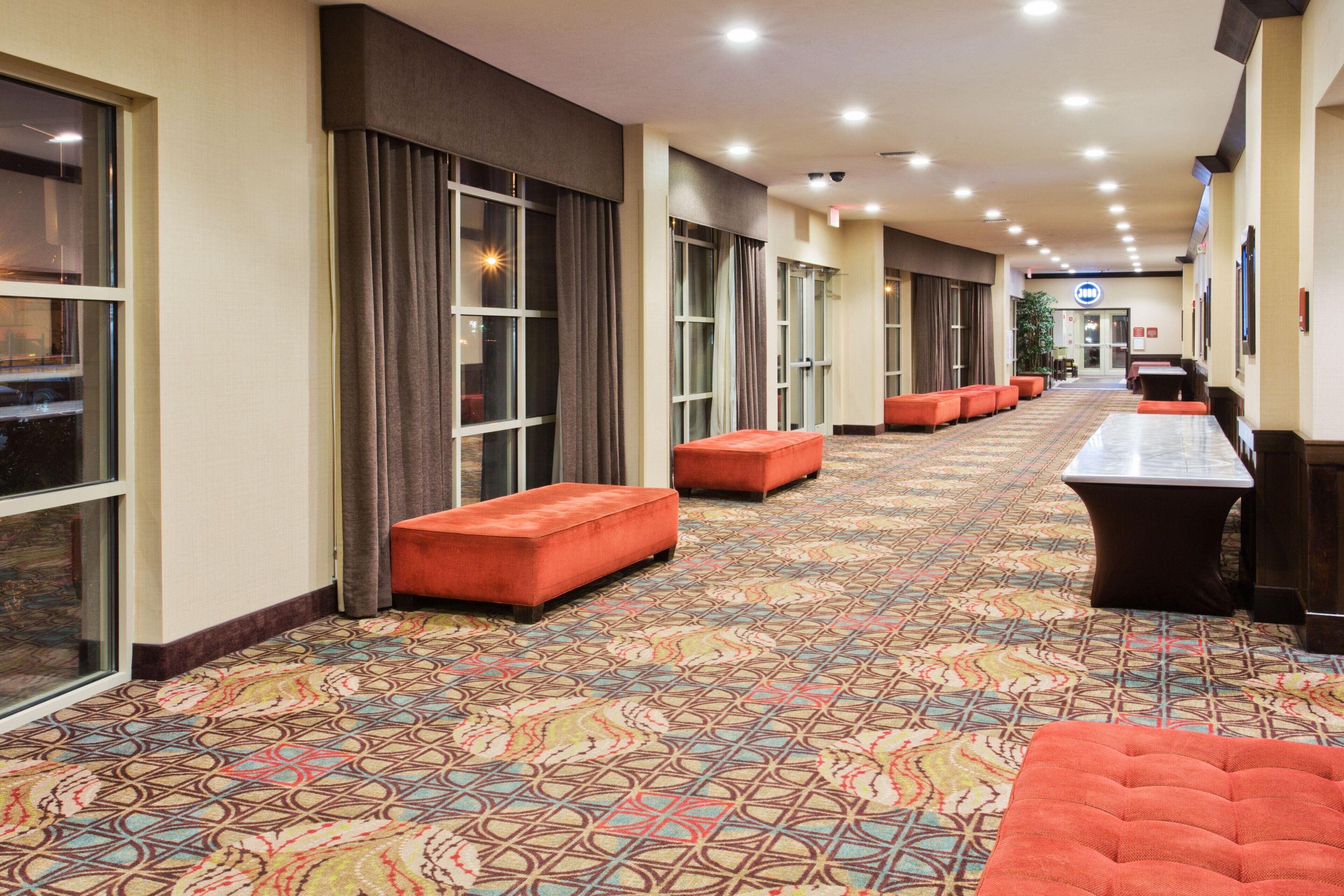 Un pasillo de hotel con alfombra estampada, zonas de descanso y un mostrador de recepción.