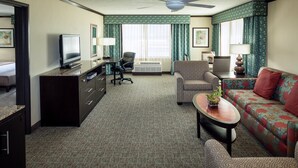 A hotel room with a television, a desk, a sofa, a chair, a ceiling fan, and a large window with curtains. - Crowne Plaza Anchorage Midtown by IHG (Anchorage)
