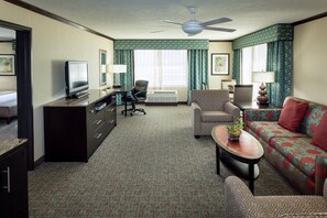 A hotel room with a television, a desk, a sofa, a chair, a ceiling fan, and a large window with curtains. - Crowne Plaza Anchorage Midtown by IHG (Anchorage)