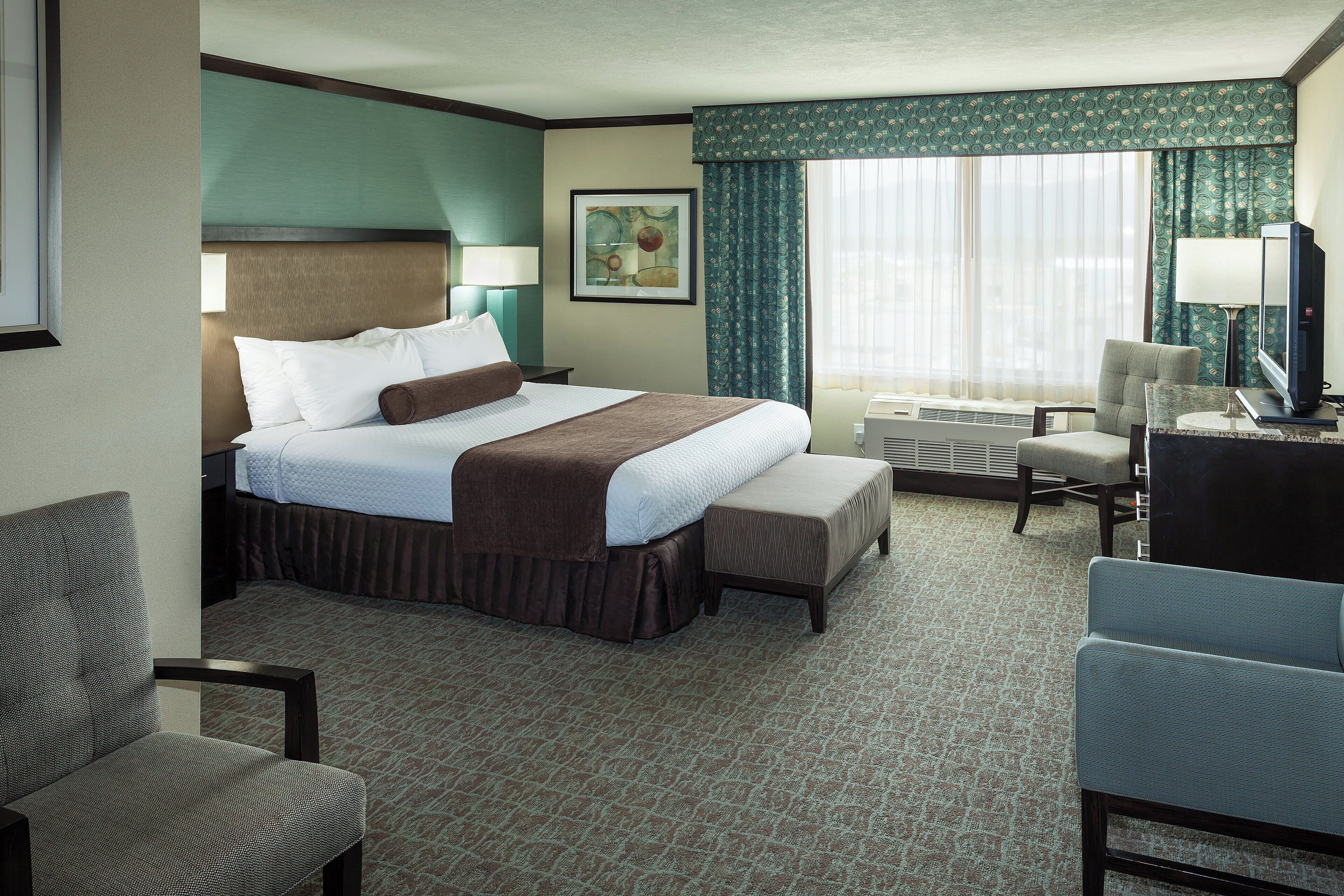 A hotel room with a bed, a desk, a chair, a television, and a window with curtains.