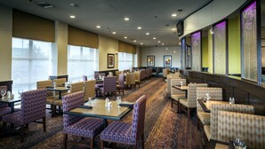 A hotel dining area with multiple tables and booths, carpeted flooring, and large windows. - Crowne Plaza Anchorage Midtown by IHG (Anchorage)