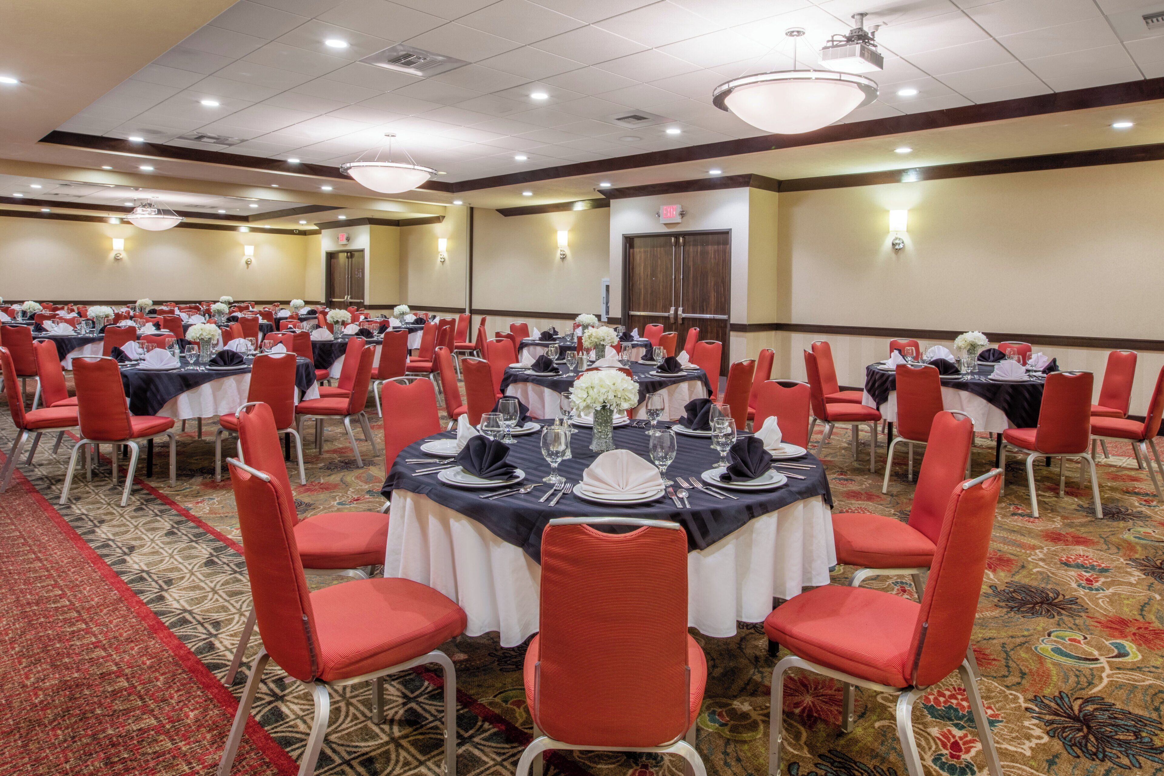 A conference room with round tables, red chairs, and white tablecloths.