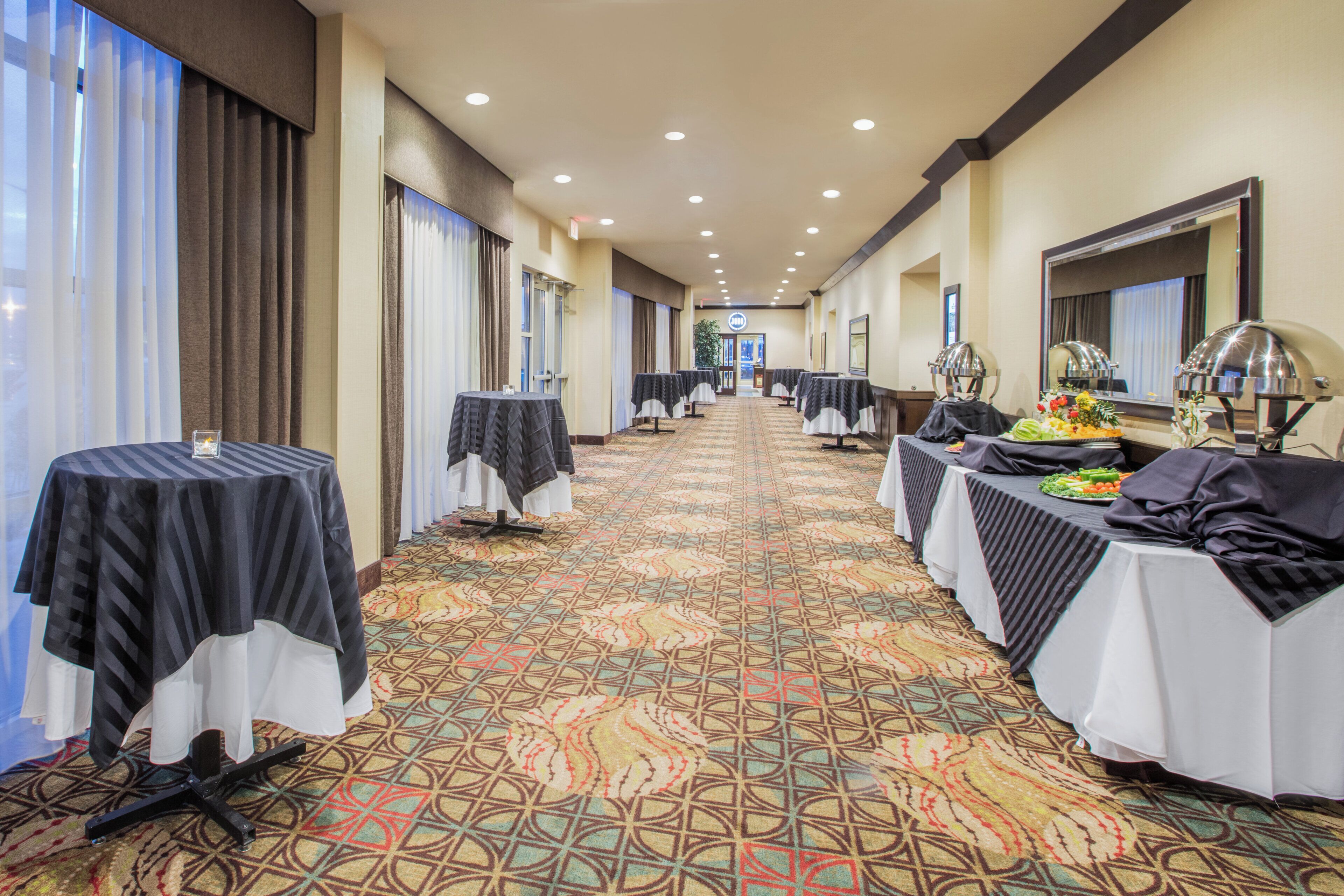 A hotel corridor with tables set up for dining, a patterned carpet, and a view of the hotel entrance.
