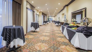 A hotel corridor with tables set up for dining, a patterned carpet, and a view of the hotel entrance.