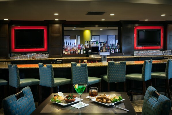 A bar area with multiple seating options, a variety of bottles, and a television screen. - Crowne Plaza Anchorage Midtown by IHG (Anchorage)