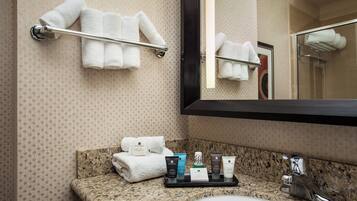 A bathroom with a granite countertop, a sink, and a mirror. There are towels on a towel rack and a tray with toiletries.