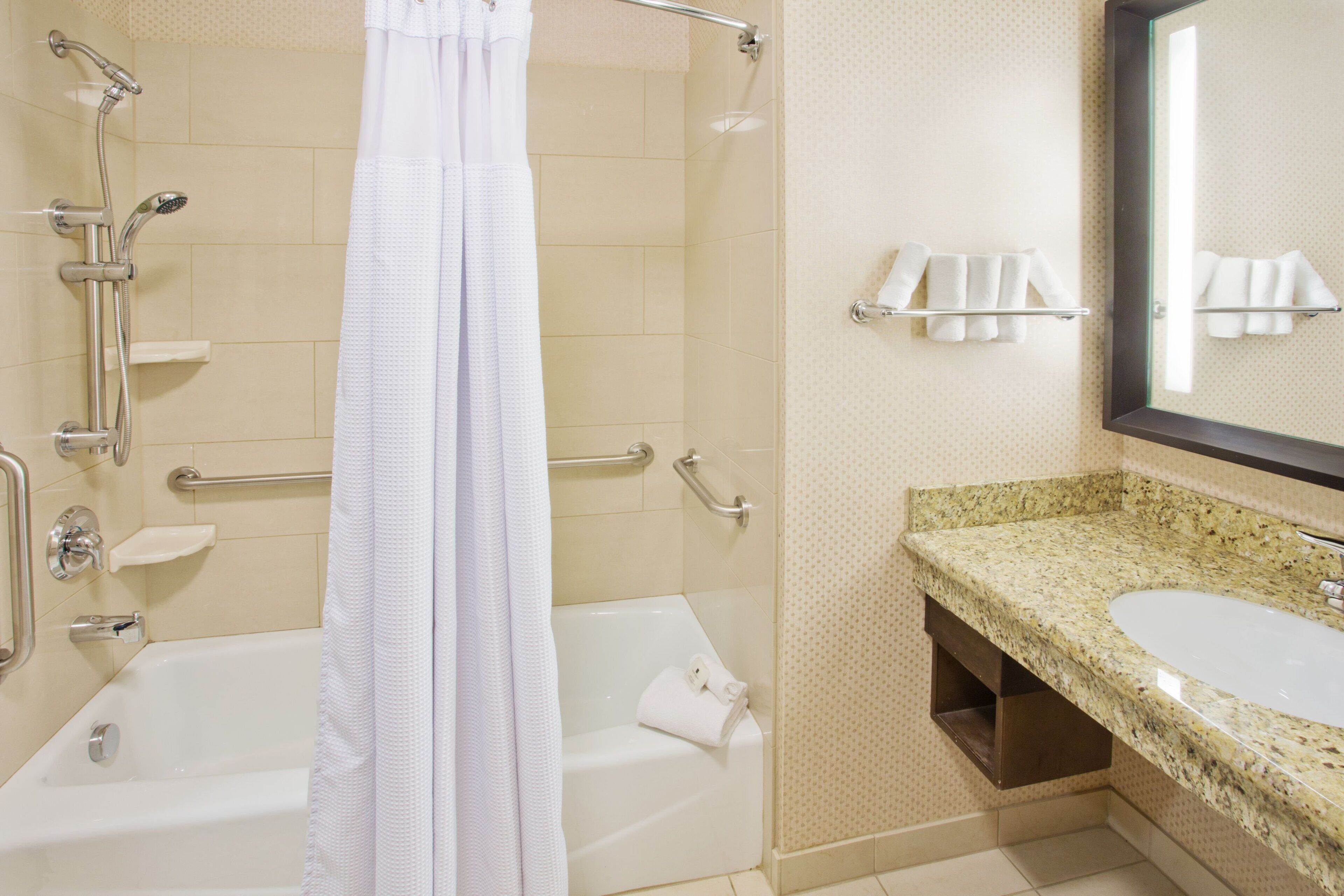 A bathroom with a bathtub, a shower with a handheld showerhead, a glass-enclosed sink, and a towel rack.