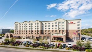 A large hotel with a central entrance, multiple floors, and a parking lot with several cars. - Crowne Plaza Anchorage Midtown by IHG (Anchorage)