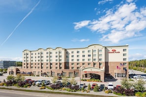 A large hotel with a central entrance, multiple floors, and a parking lot with several cars. - Crowne Plaza Anchorage Midtown by IHG (Anchorage)