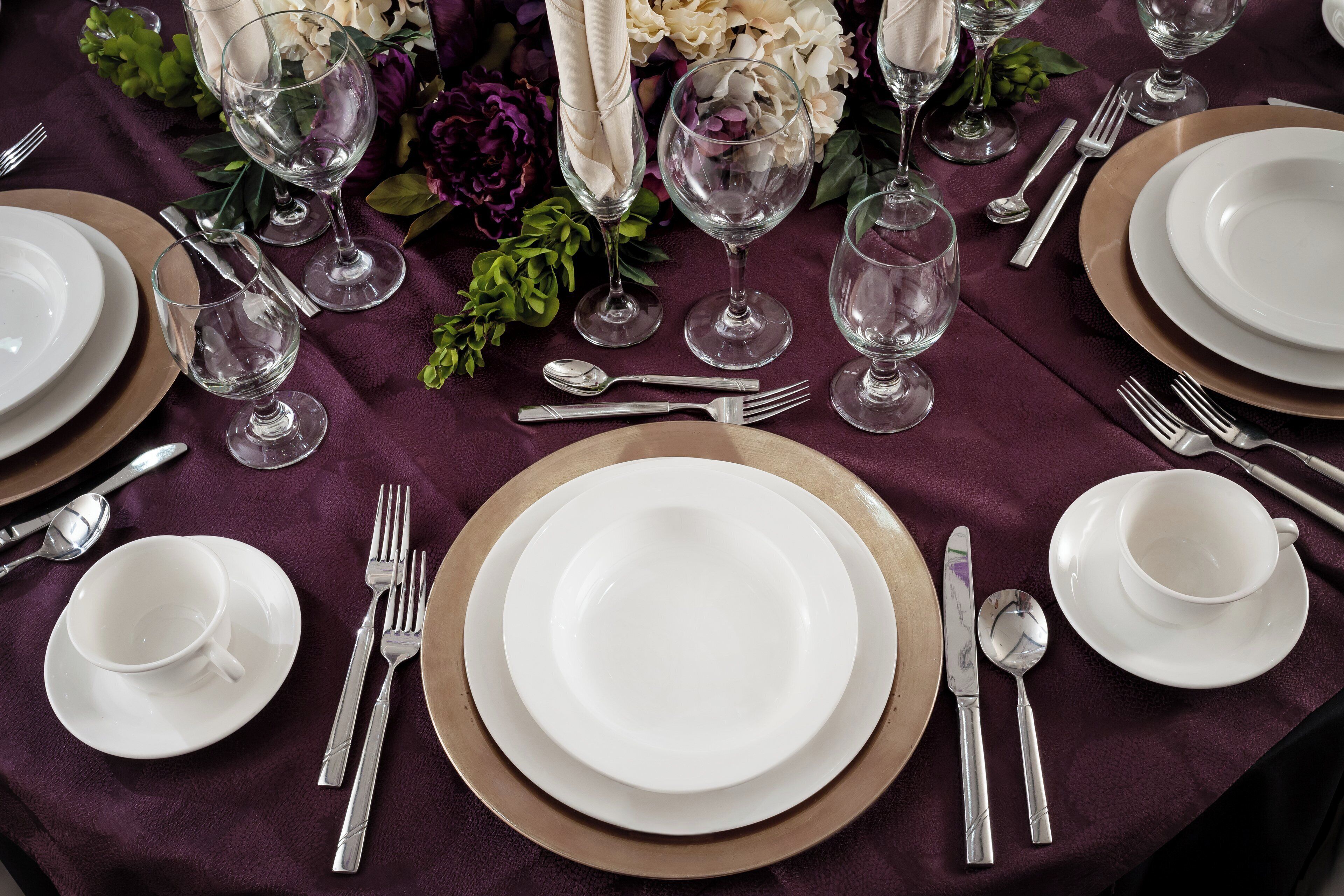 Una mesa puesta para comer, con platos blancos, cubiertos y copas de cristal.