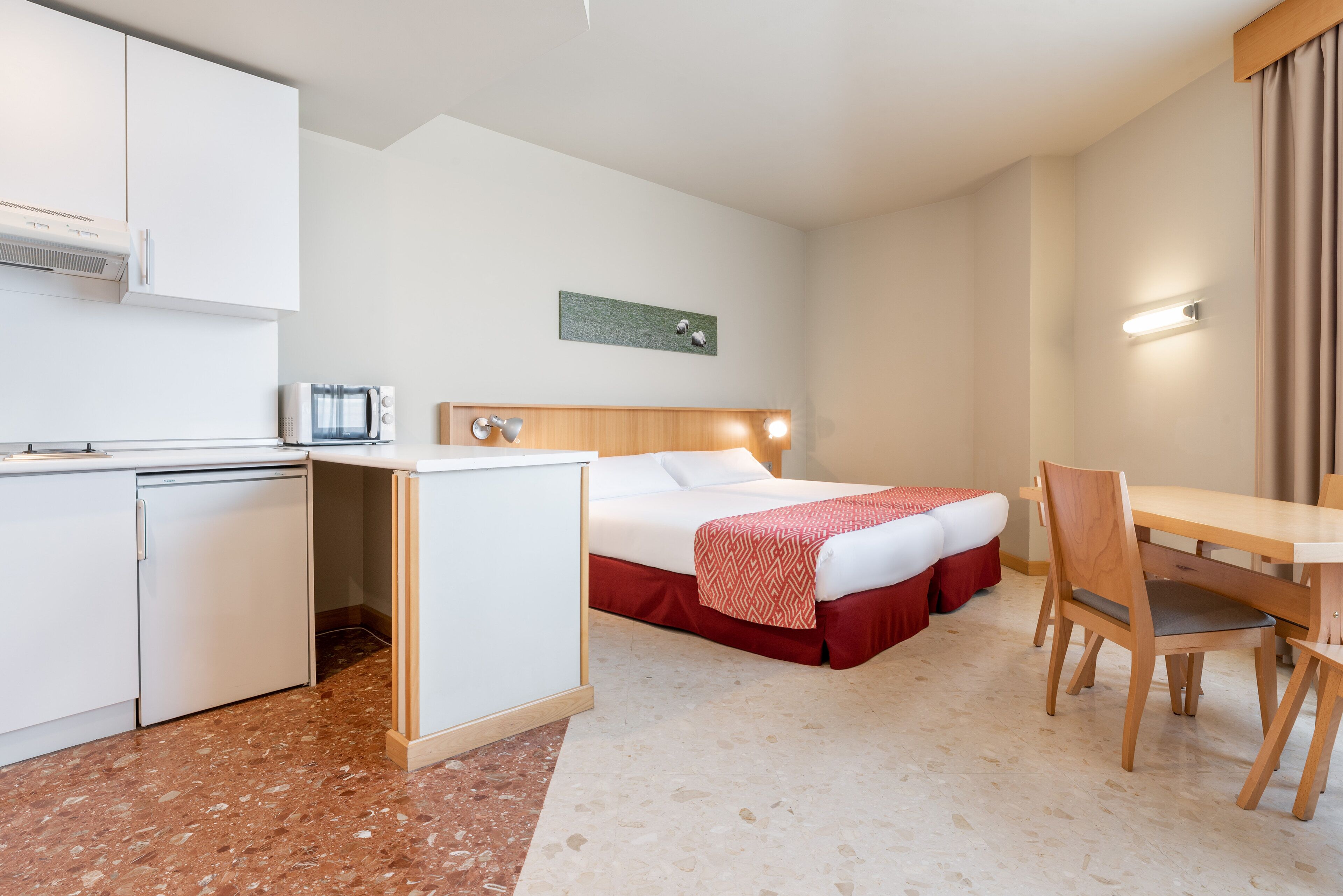 Ein Hotelzimmer mit einem Bett, einem Schreibtisch, einem Stuhl, einer Mikrowelle, einem Kühlschrank und einer kleinen Küchenzeile.