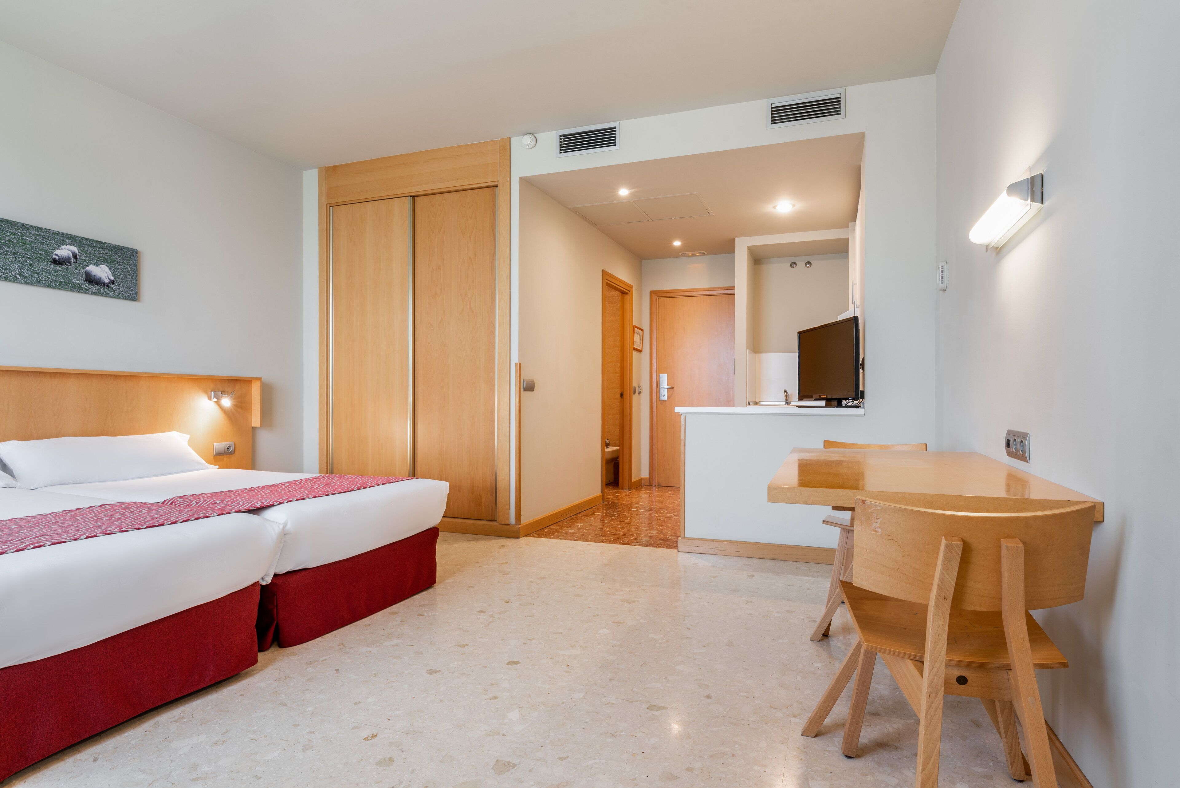 Habitación de hotel con cama, escritorio y silla. Se ve una puerta que conduce a otra habitación y un baño.