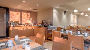 Een moderne eetruimte met houten tafels, stoelen en een bar in het midden met een koffieapparaat.