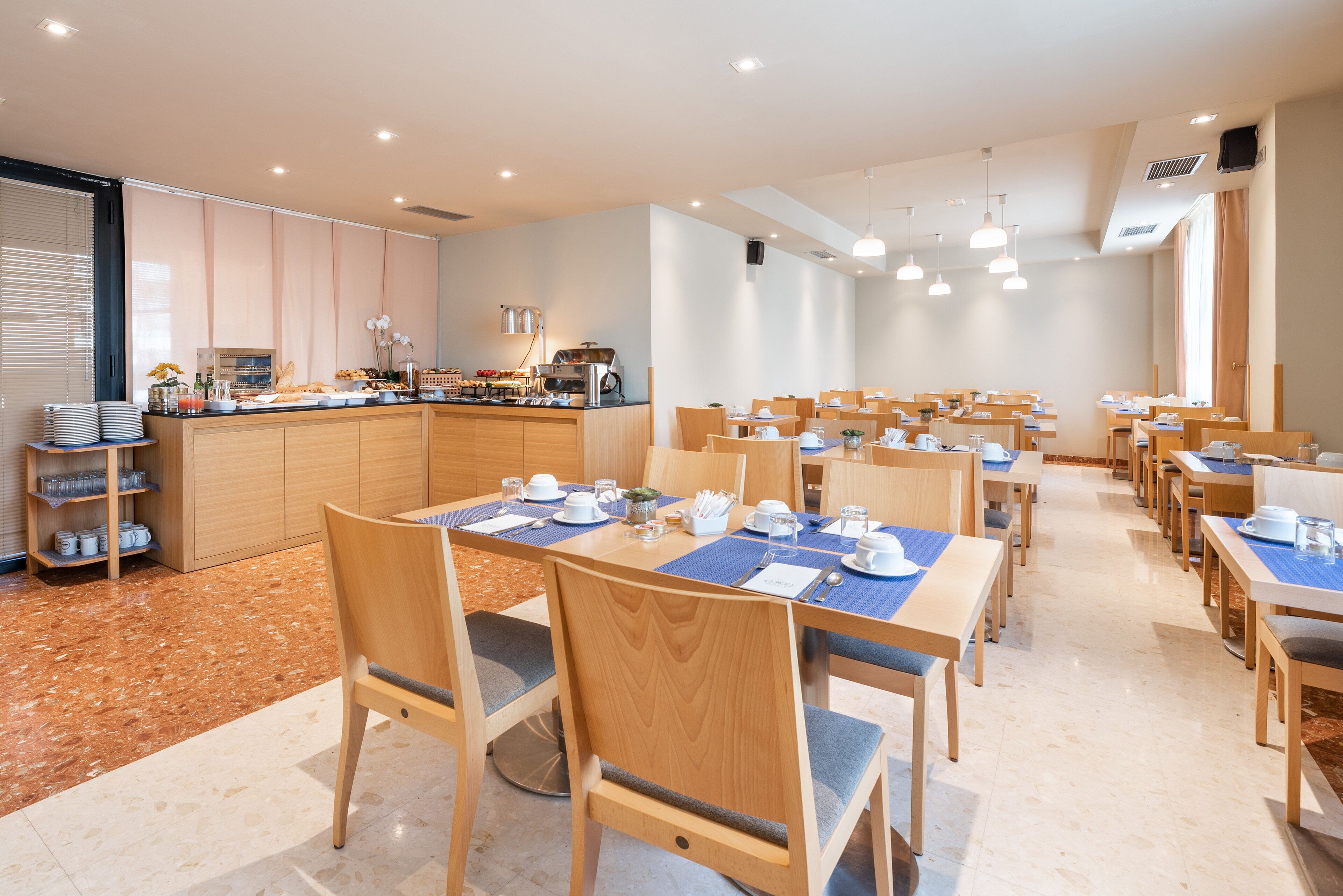Een moderne eetruimte met houten tafels en stoelen, een buffet en een keuken op de achtergrond.