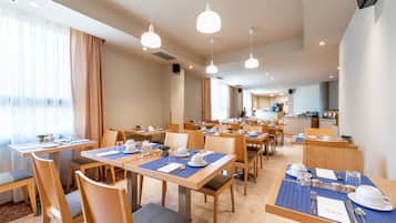 Comedor de hotel con varias mesas dispuestas para el desayuno, sillas de madera y lámparas colgantes.