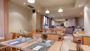 Ein Hotel-Speisesaal mit mehreren für ein Frühstück gedeckten Tischen, ausgestattet mit Besteck, und einer Küche im Hintergrund.