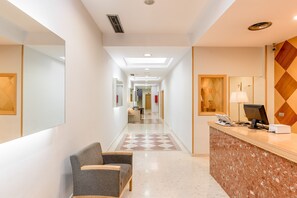 Zona de recepción de un hotel con mostrador de recepción, una silla, mostrador de registro y un pasillo que conduce a otras habitaciones.
