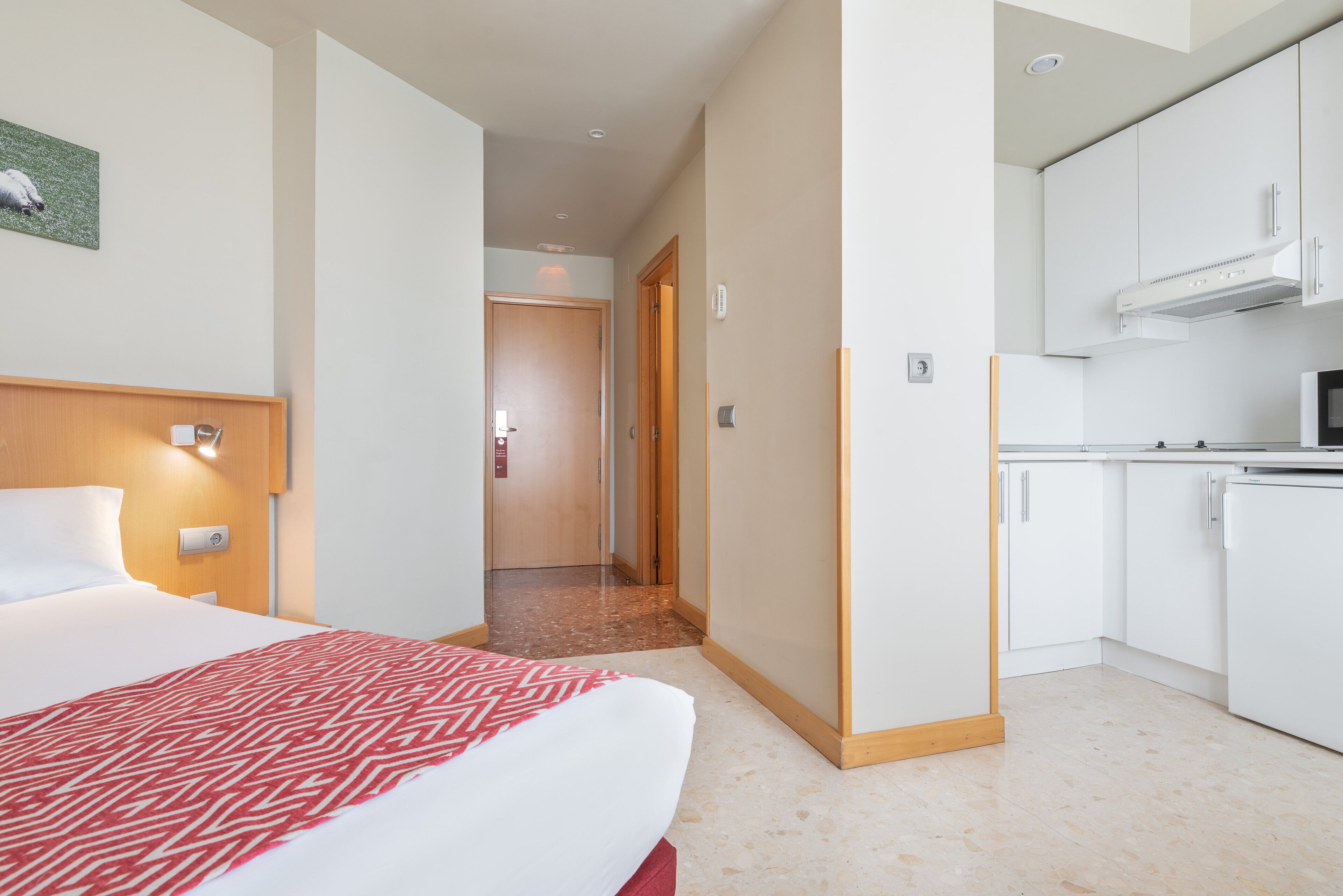 A hotel room with a bed, a kitchenette, and a hallway leading to another room.