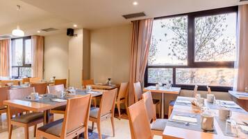Comedor con varias mesas y sillas, dispuesto con vajilla y tazas de café.