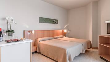A modern hotel room with two beds, a small desk with a vase of flowers, and a wall-mounted artwork.