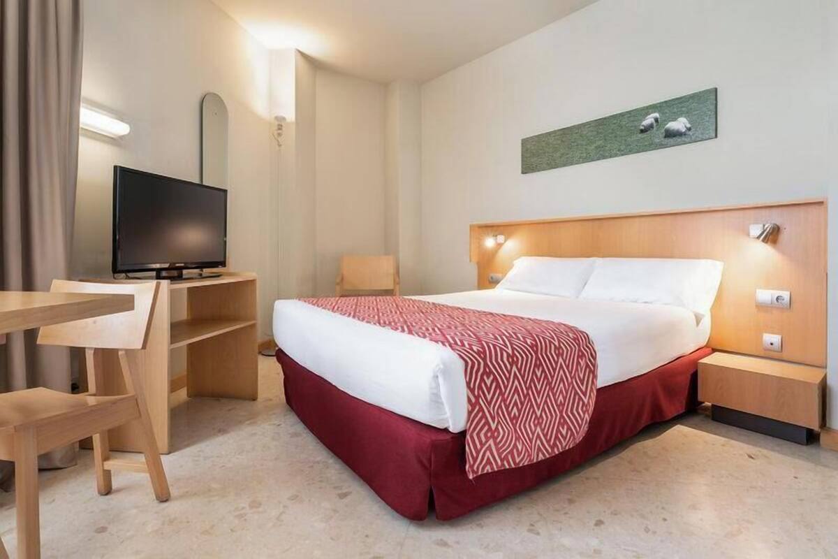 A hotel room with a bed, a desk, a television, and a wall-mounted artwork.