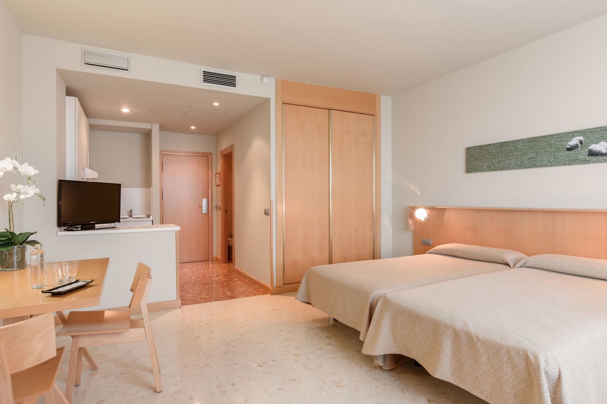 A hotel room with a bed, a desk with a chair, a television, and a painting on the wall.