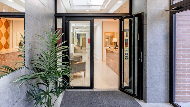 Eine Hotlellobby mit einer Rezeption, einer Sitzecke und einem Glastür-Eingang.