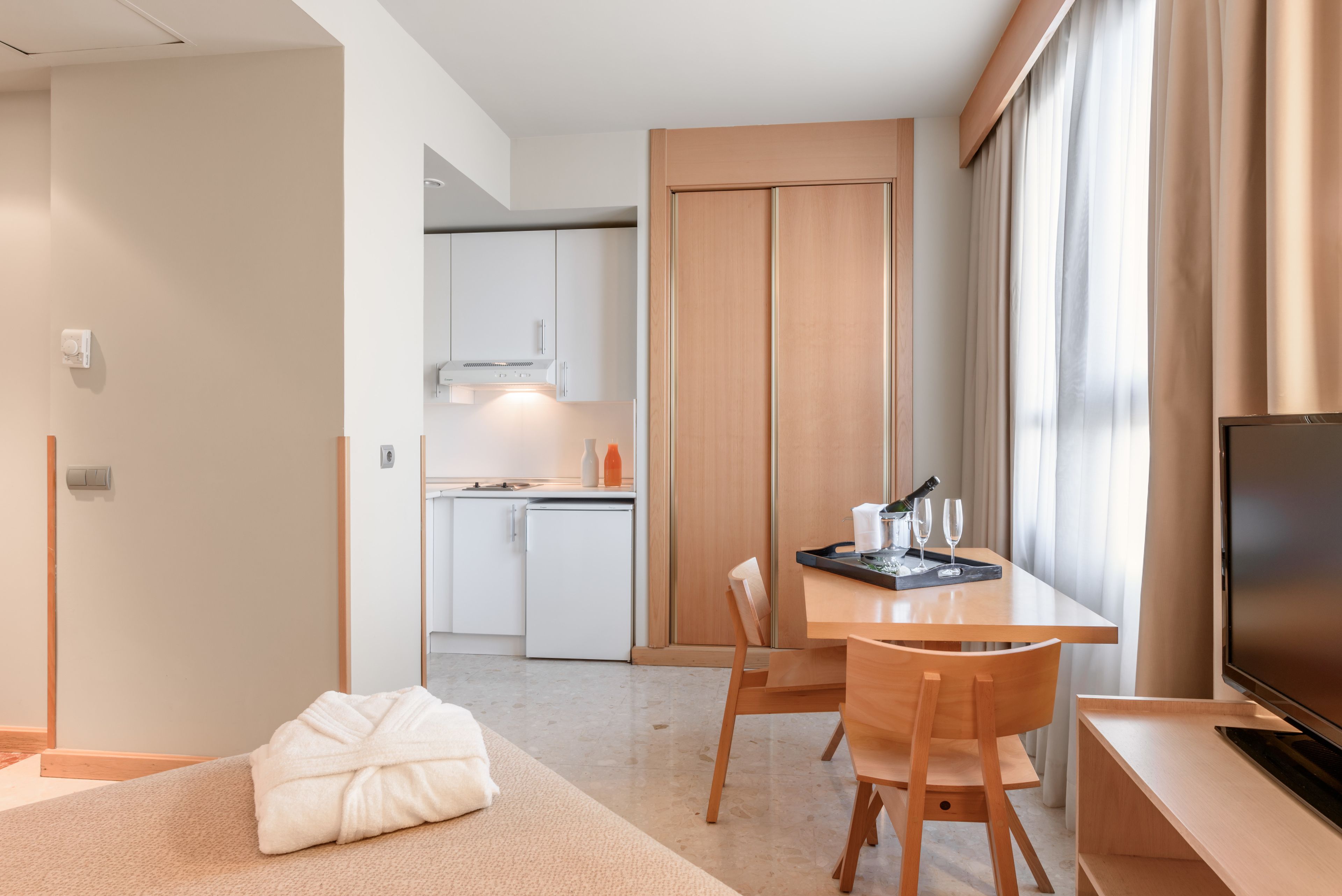 A modern hotel room with a dining area, kitchenette, and a TV.