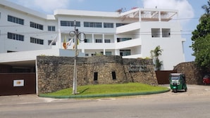 A modern building with a stone wall entrance, a flagpole with flags, and a green vehicle parked in front.