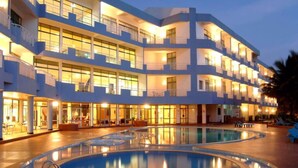 A multi-story hotel with a pool area, featuring a large pool with a circular design and a separate smaller pool.