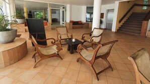 A spacious lobby with a seating area featuring wooden chairs and a coffee table, a large potted plant, and a staircase leading to an upper level.