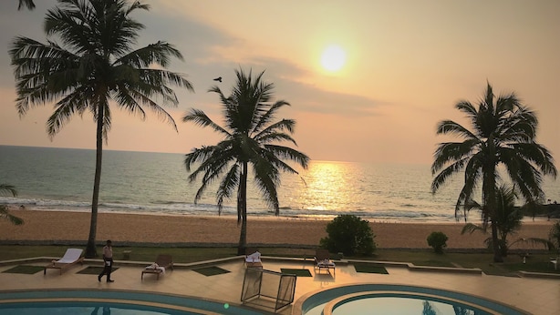 A pool area with palm trees and a view of the ocean at sunset.