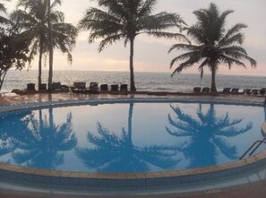 Piscina cercada por palmeiras com vista para o oceano.