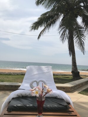 Uma espreguiçadeira à beira-mar com uma toalha, um copo de bebida vermelha e um vaso com flores, com vista para o oceano.