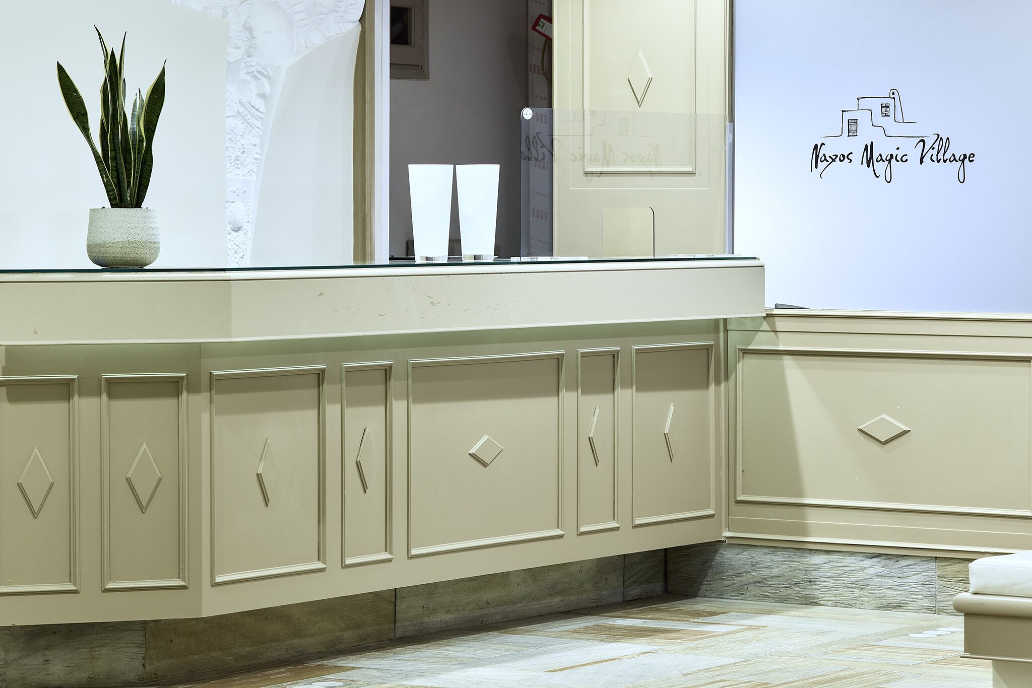 A bathroom with a beige vanity, a potted plant, and a wall decal reading "Najos Magic Village."